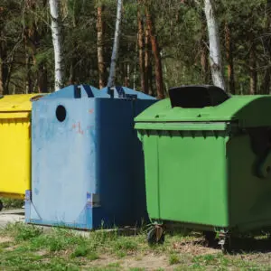 Yellow, blue, green dumpsters in a forest.