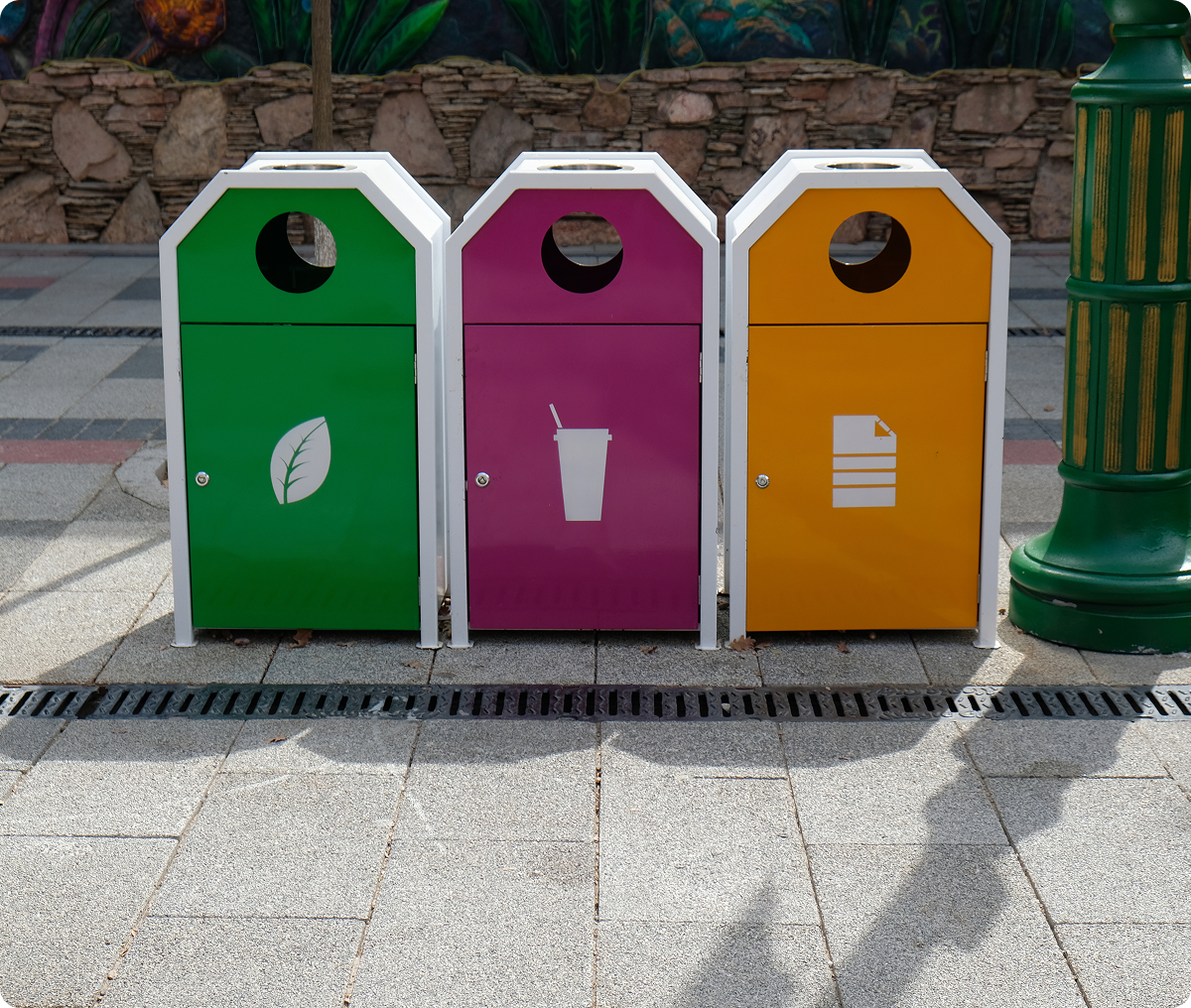Colorful recycling bins on a paved walkway.